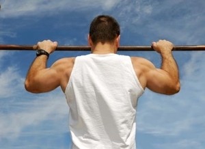 Image of a male client performing pull-ups outdoors as part of a fitness program.